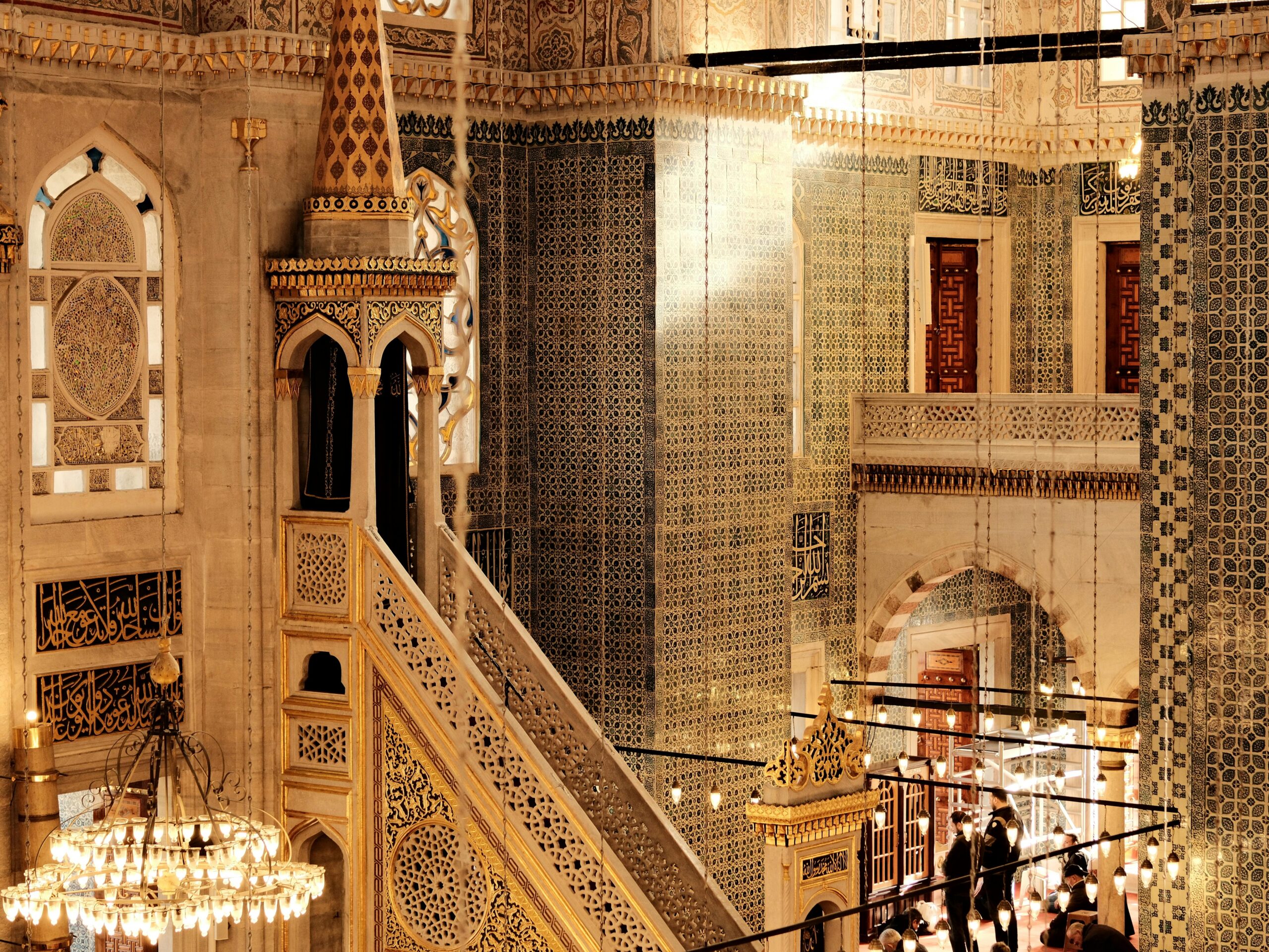 Intricate architecture and Islamic art inside a traditional mosque, filled with golden and blue tile designs.